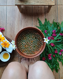 Bacia de escalda pés, com bolo de gude, toalhas brancas e flores amarelas ao lado